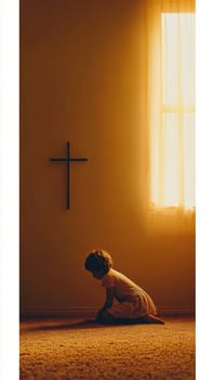Young girl is silhouetted kneeling on the floor in prayer with the warm light from a window behind her illuminating the wall with the cross