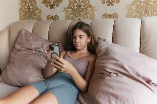 A girl is laying on a bed with a cell phone in her hand. She is smiling and she is enjoying herself