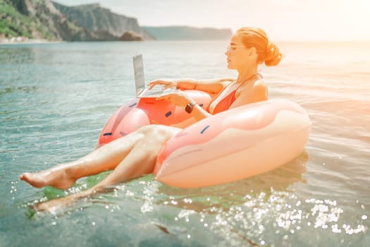 Woman laptop sea. Freelancer woman in sunglases floating on an inflatable big pink donut with a laptop in the sea. People summer vacation rest lifestyle concept