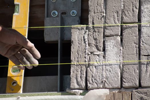 Builder aligning bricks on wall with level, tools in background, Concept of precision in construction work,