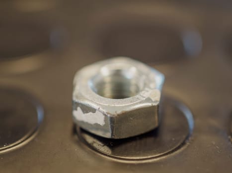 Chipped metal hex nut on a dark surface with circular indentations, showcasing industrial details. Close up highlights texture and shine, evoking engineering and manufacturing