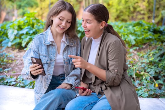 two young friends pointing at something while browsing social media on the phone.