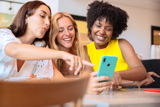 Three young friends pointing at something while browsing social media on the phone.