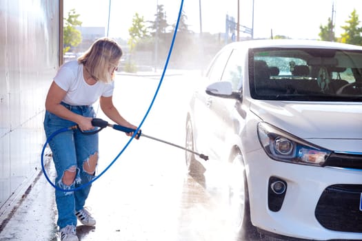 Image, portrait of a young, smiling, attractive woman washing a car in a car wash, car wash, foam cleaning, pressure water