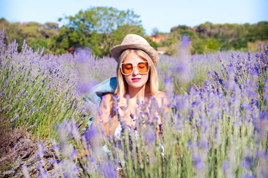 A happy young Caucasian woman wearing sunglasses stands in a vibrant lavender field, posing for the camera, capturing a moment of carefree joy at the beauty of nature.