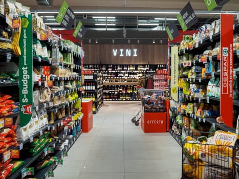 Cremona, Italy September 26th 2024 A modern supermarket aisle with a shopping cart standing between shelves full of various goods