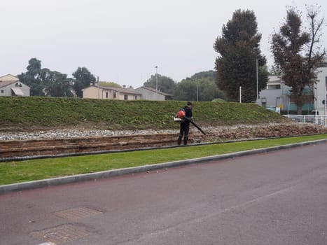 Cremona, Italy September 26th 2024 A gardener is taking care of a park in autumn, using a leaf blower to gather the fallen leaves