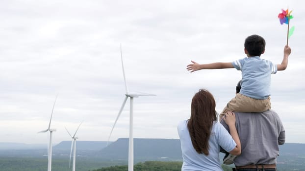 Concept of progressive happy family enjoying their time at the wind turbine farm. Electric generator from wind by wind turbine generator on the country side with hill and mountain on the horizon.