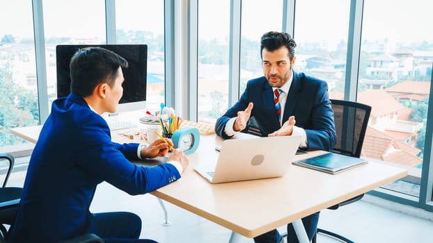 Two business people talk project strategy at office meeting room. Businessman discuss project planning with colleague at modern workplace while having conversation and advice on financial report. Jivy