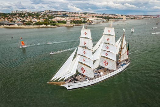 Aerial drone view of tall ships with sails sailing in Tagus river towards the Atlantic ocean in Lisbon, Portugal