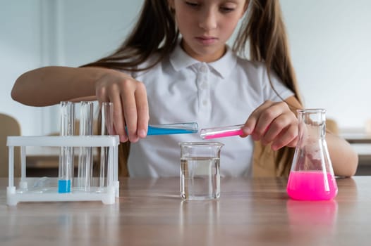 A schoolgirl conducts experiments in a chemistry lesson. Girl pouring colored liquids from a beaker