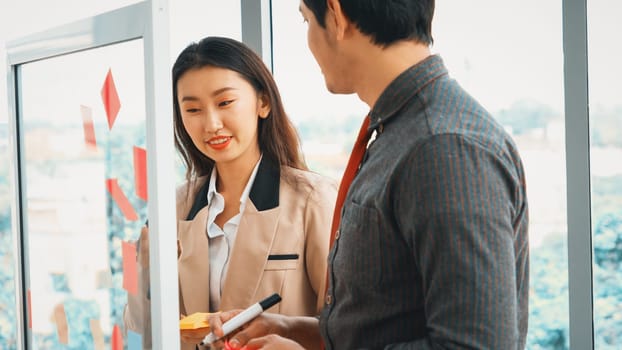 Business people work on project planning board in office and having conversation with coworker friend to analyze project development . They use sticky notes posted on glass to make it organized. Jivy