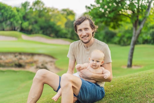 Dad and baby sit on the grass in the park.
