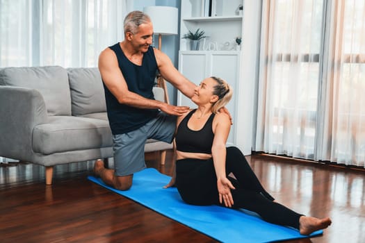 Happy active senior couple in sportswear being supportive and assist on yoga posture together at home. Healthy senior man and woman lifestyle with yoga exercise. Clout