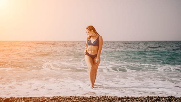 Beach vacation. Hot beautiful woman in sunhat and bikini standing with her arms raised to her head enjoying looking view of beach ocean on hot summer day.