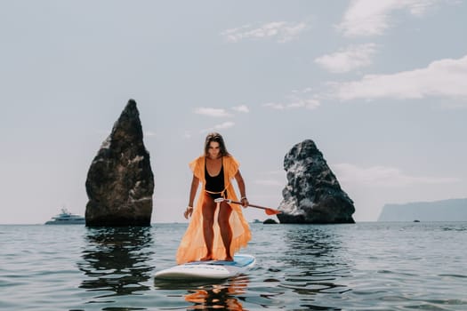 Close up shot of beautiful young caucasian woman with black hair and freckles looking at camera and smiling. Cute woman portrait in a pink bikini posing on a volcanic rock high above the sea