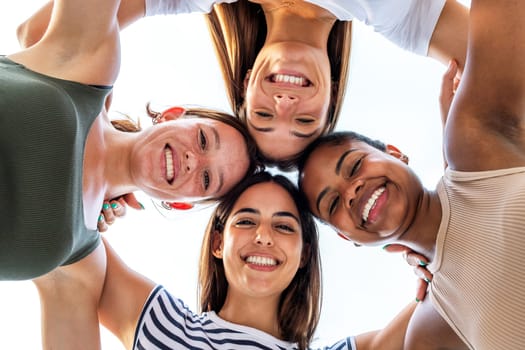 Low angle view of multiracial girl friends heads in circle. College student female friends smiling looking at camera. Friendship and team spirit concept.