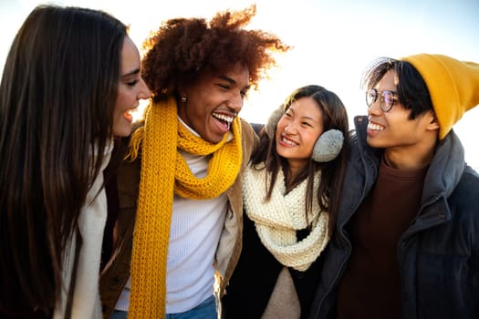 Multiethnic college student friends enjoying sunny winter day together. Young happy people embracing having fun outdoors talking and laughing.Lifestyle concept.