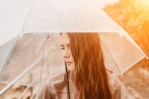 Woman rain park. Happy woman portrait wearing a raincoat with transparent umbrella outdoors on rainy day in park near sea. Girl on the nature on rainy overcast day