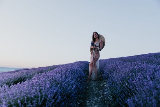 Close up portrait of young beautiful woman in a white dress and a hat is walking in the lavender field and smelling lavender bouquet.