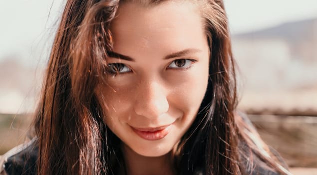 Happy young smiling woman with freckles outdoors portrait. Soft sunny colors. Outdoor close-up portrait of a young brunette woman and looking to the camera, posing against nature background.