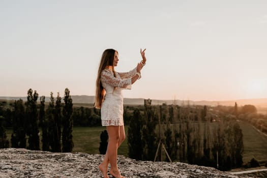 Romantic beautiful bride in white dress posing with sea and mountains in background. Stylish bride standing back on beautiful landscape of sea and mountains on sunset