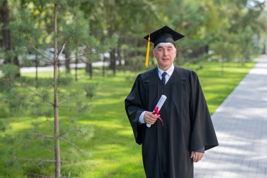 Serious old man in graduation gown holding diploma outdoors