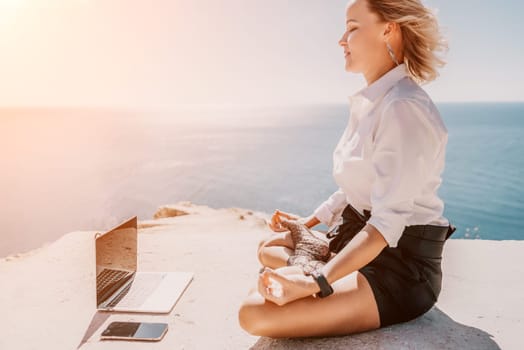 Happy girl doing yoga with laptop working at the beach. beautiful and calm business woman sitting with a laptop in a summer cafe in the lotus position meditating and relaxing. freelance girl remote work beach paradise