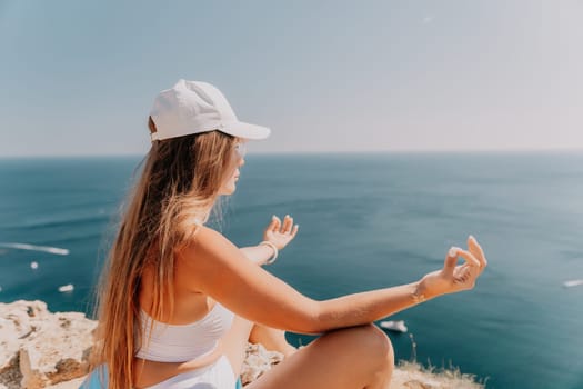 Woman meditating in yoga pose silhouette at the ocean, beach and rock mountains. Motivation and inspirational fit and exercising. Healthy lifestyle outdoors in nature, fitness concept.