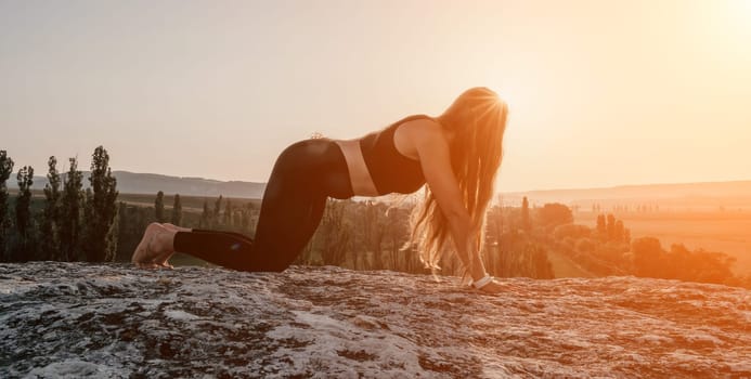 Well looking middle aged woman with long hair, fitness instructor in leggings and tops doing stretching and pilates on the rock near forest. Female fitness yoga routine concept. Healthy lifestyle.