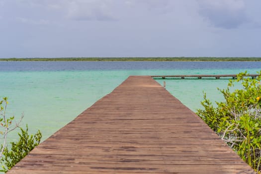 Wooden pier extending into the turquoise waters of Bacalar Lake, Mexico. Peaceful and scenic tropical destination. Travel, relaxation, and nature concept.