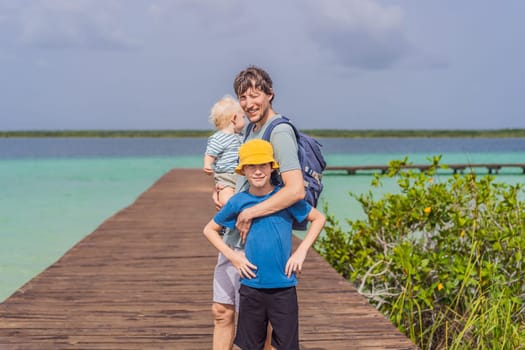Father with his toddler and teenage sons exploring wooden pier over the turquoise waters of Bacalar Lake, Mexico. Peaceful tropical travel destination concept.