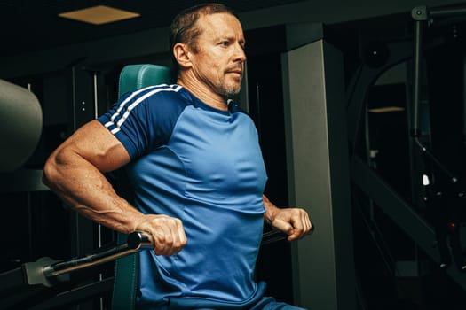 Senior man doing exercises for arms in a training machine in gym