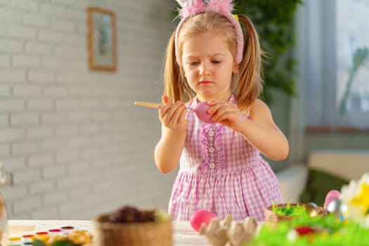 Toddler girl with bunny ears coloring eggs for Easter