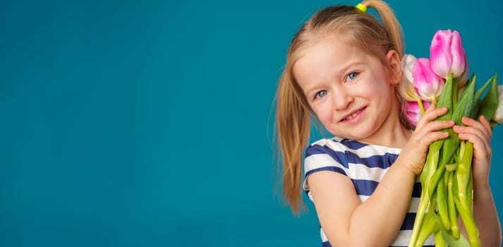 Smiling little blonde girl with tulips bouquet against blue background