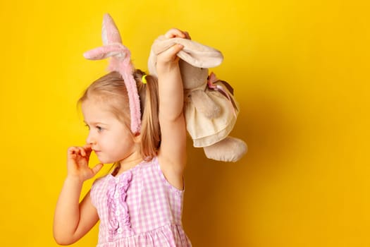 Little girl holding her bunny toy against yellow background