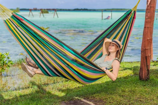 Female tourist sitting in hammock against background of turquoise waters of Lake Bacalar. Family bonding, summer vacation, and outdoor fun in Quintana Roo, Mexico concept.