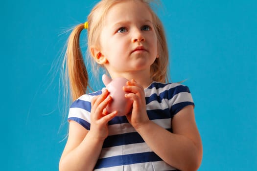 Little girl with piggy bank moneybox against blue background