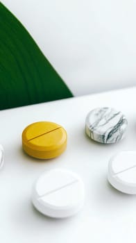 Yellow pill stands out among white ones on a white surface with a green leaf in the background, perfect for illustrating uniqueness and diversity