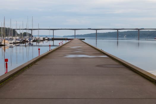 a wooden jetty or jetty in the water near vejle in denmark with the harbour and boats with a bridge in the background