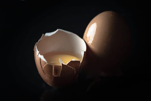 View of Egg yolk in Broken raw chicken eggshell and Fresh chicken egg (Hen egg) on Black background. Fresh eggs from the farmer, Natural organic healthy food concept, Space for text, Selective focus.