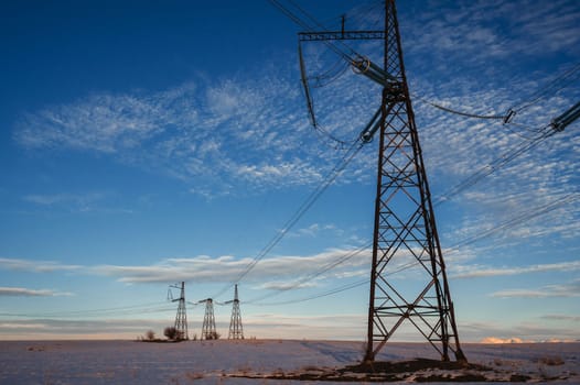 High-voltage power transmission line with towers in the field in winter at sunset in the evening