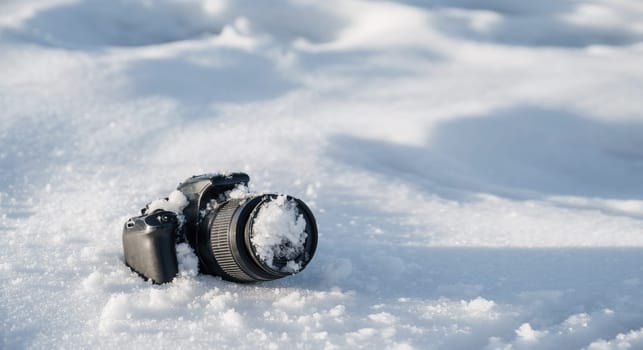 professional digital slr photo camera with frost lens lies in a snowdrift in winter in the snow with copy space