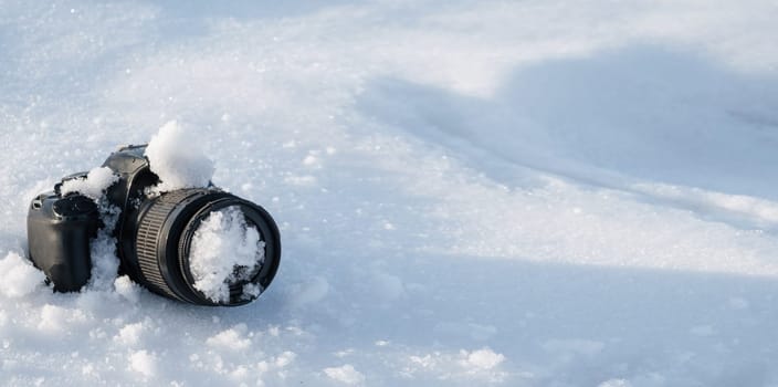 professional digital slr photo camera with frost lens lies in a snowdrift in winter in the snow with copy space