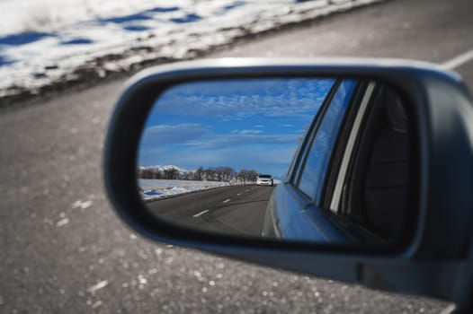 reflection of a beautiful winter landscape with a road and mountains in the snow in rearview mirror of the car. The concept of festive holiday winter travel