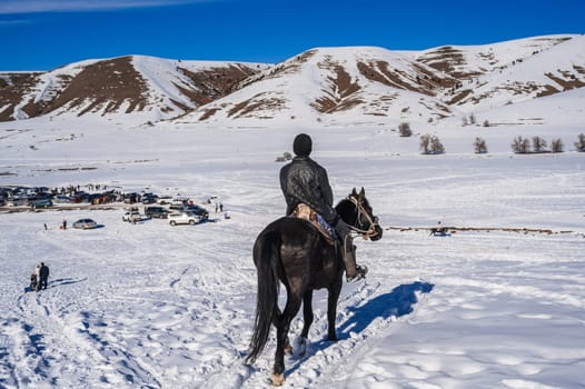 The back of a Kazakh teenager on a horse in the steppes of Kazakhstan in winter. Shymkent, Kazakhstan - January 27, 2024