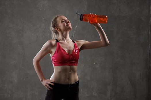 sporty woman pouring water from bottle on herself after workout on grey concrete background. sport concept