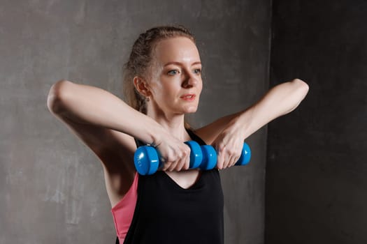A woman exercises with blue dumbbells in a fitness studio. She performs a strength exercise focusing on the upper body, concept of doing sports