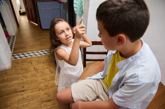 A cheerful young girl gestures energetically while talking to her brother indoors, illustrating sibling interaction and communication.