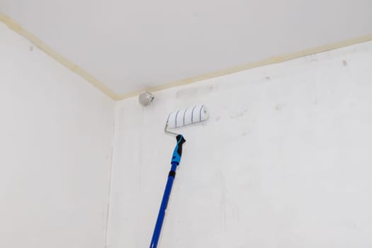 Male hand painting wall with paint roller. Painting apartment, renovating with white color paint